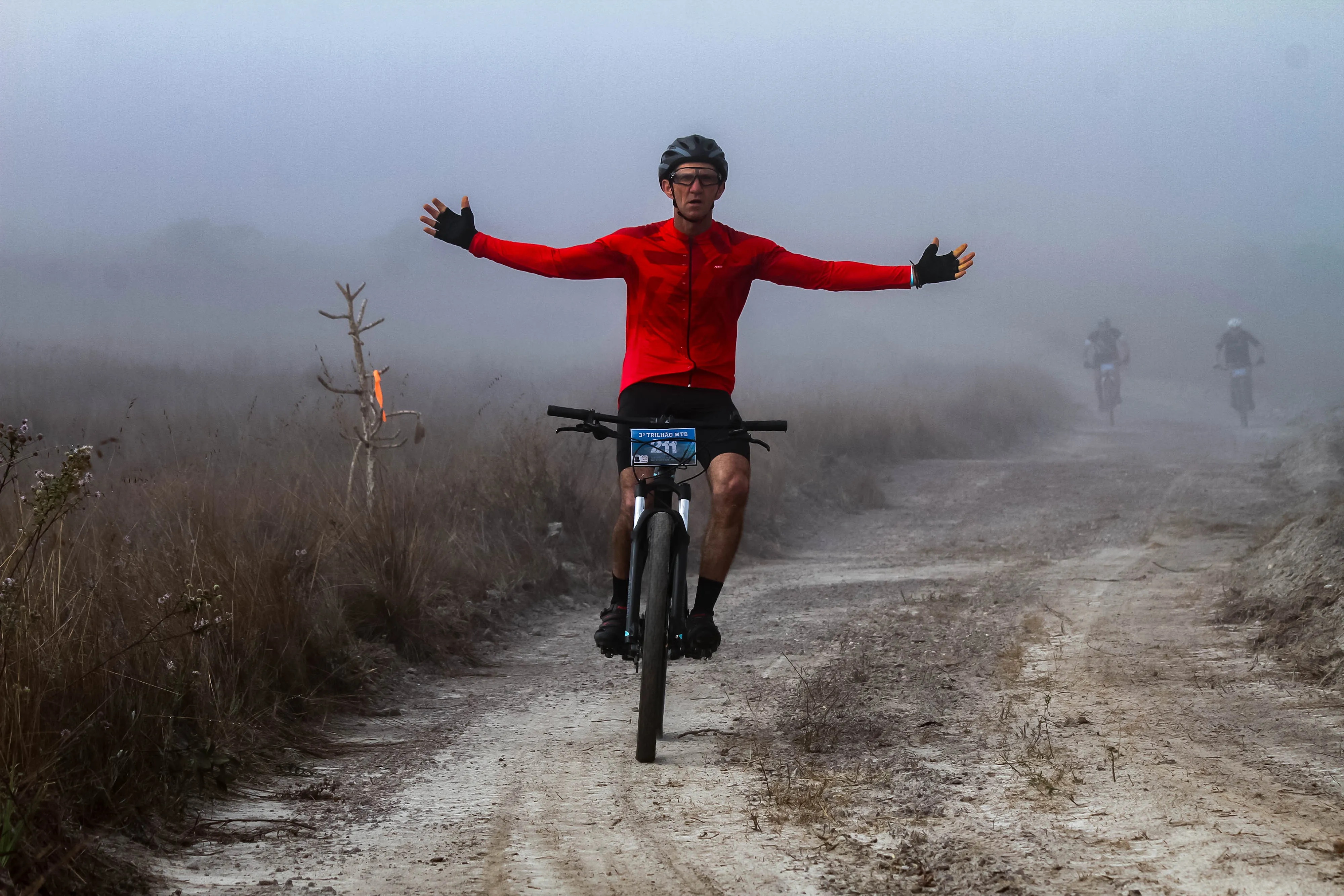 Atleta com braços abertos celebrando na névoa da Serra de São Thomé das Letras