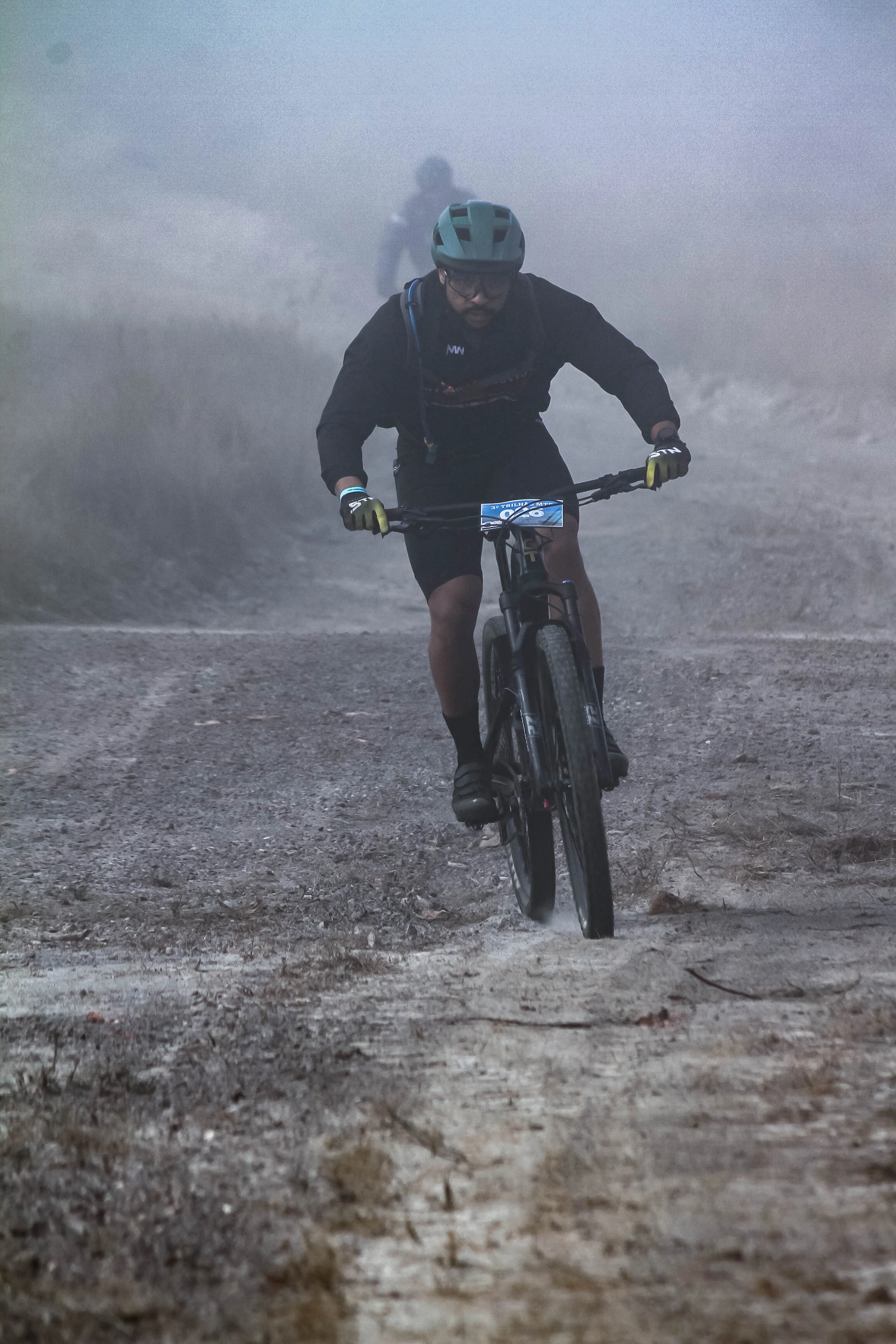 Atleta acelerando em trilha poeirenta envolto em névoa na serra
