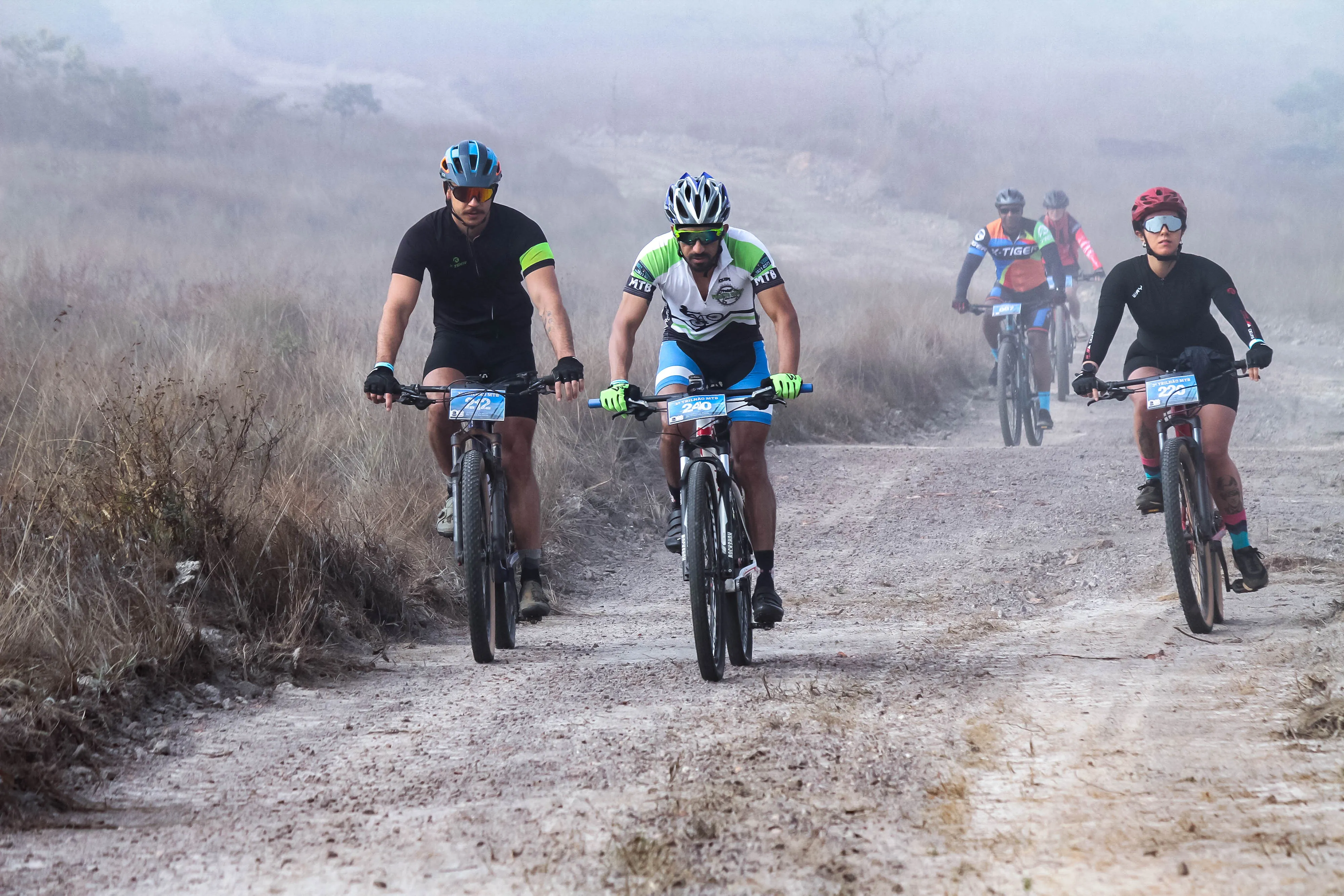 Grupo de ciclistas pedalando juntos na estrada de terra na névoa