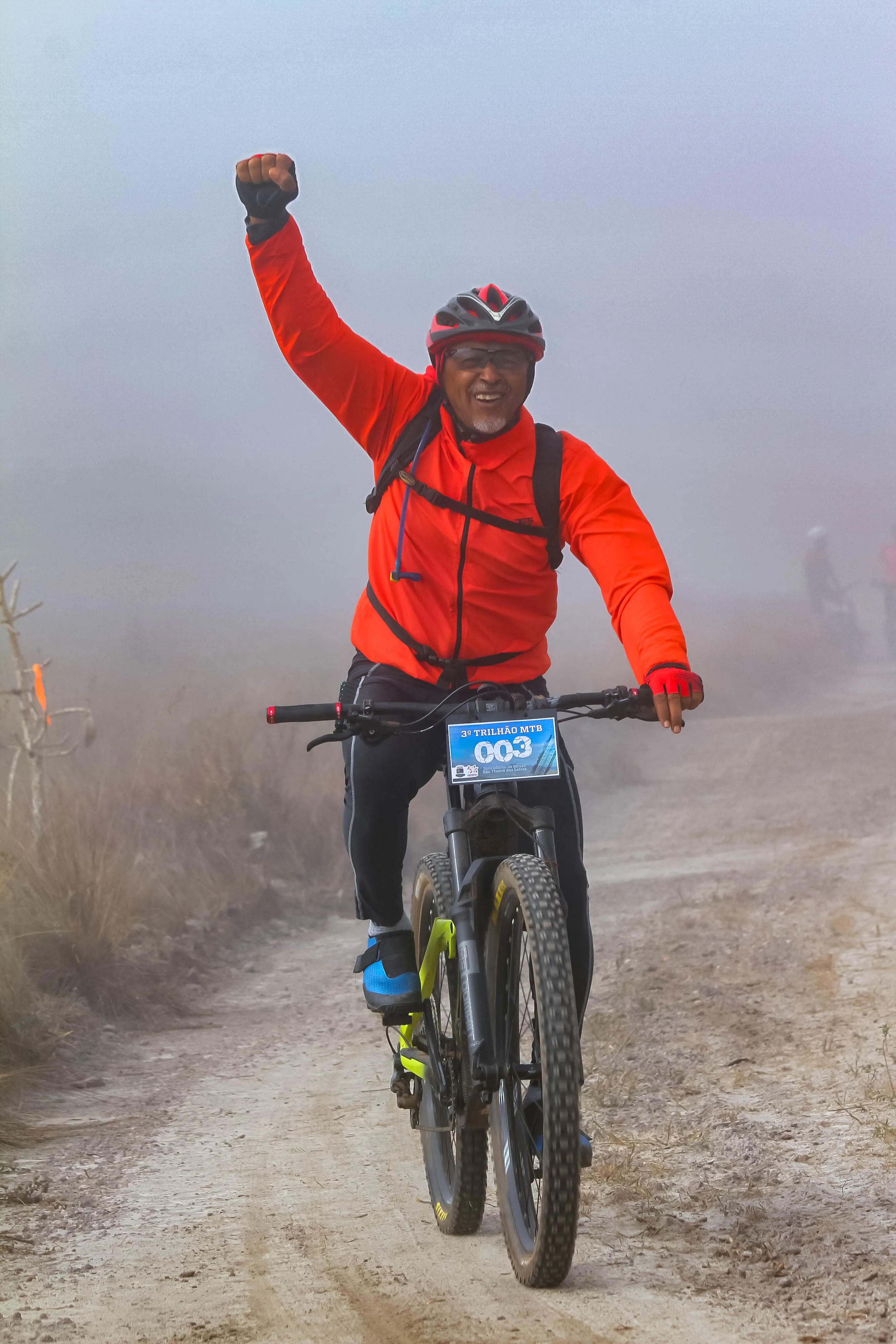 Atleta erguendo o punho em sinal de vitória na névoa da trilha