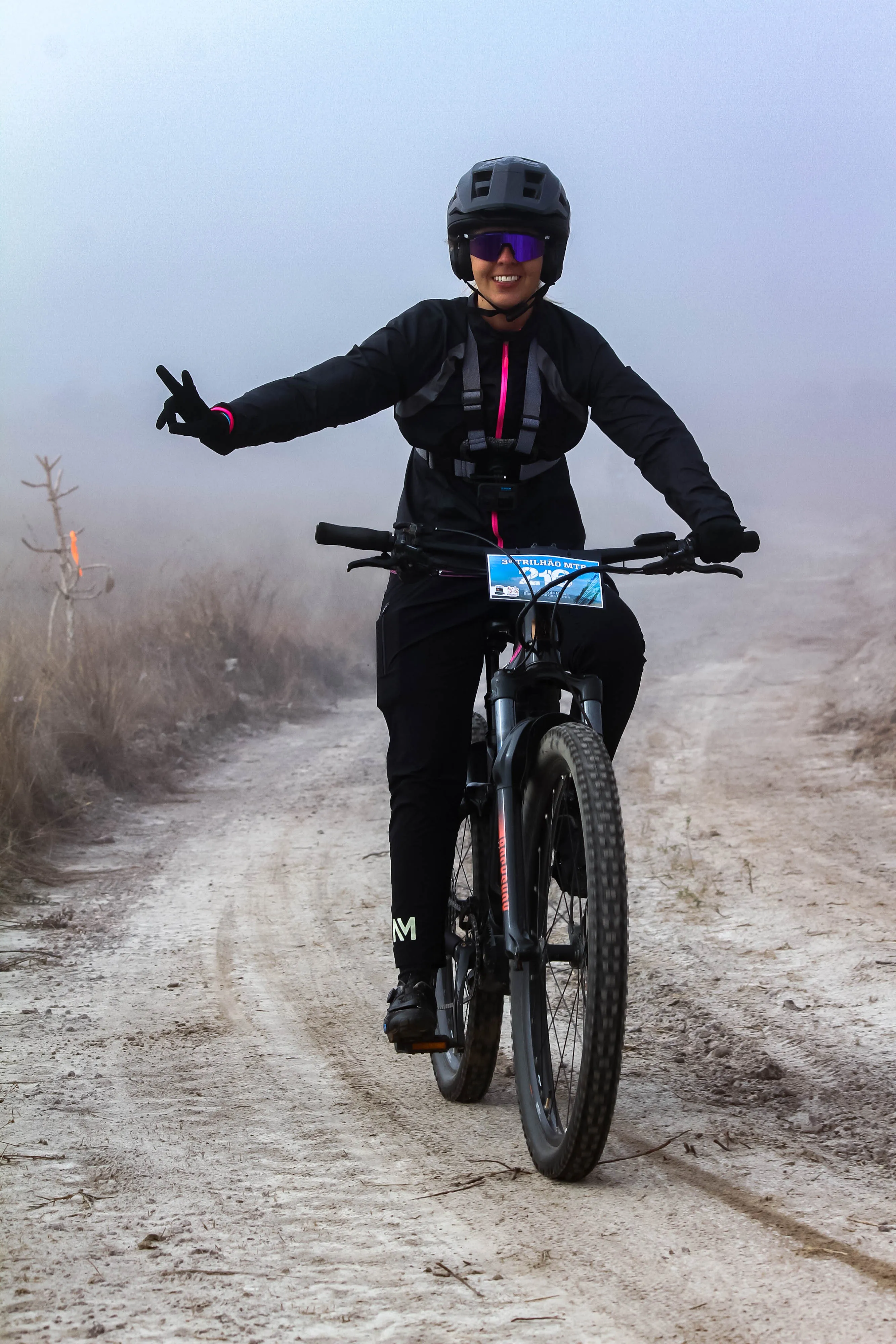 Atleta feminina fazendo sinal de paz sorrindo na névoa da trilha