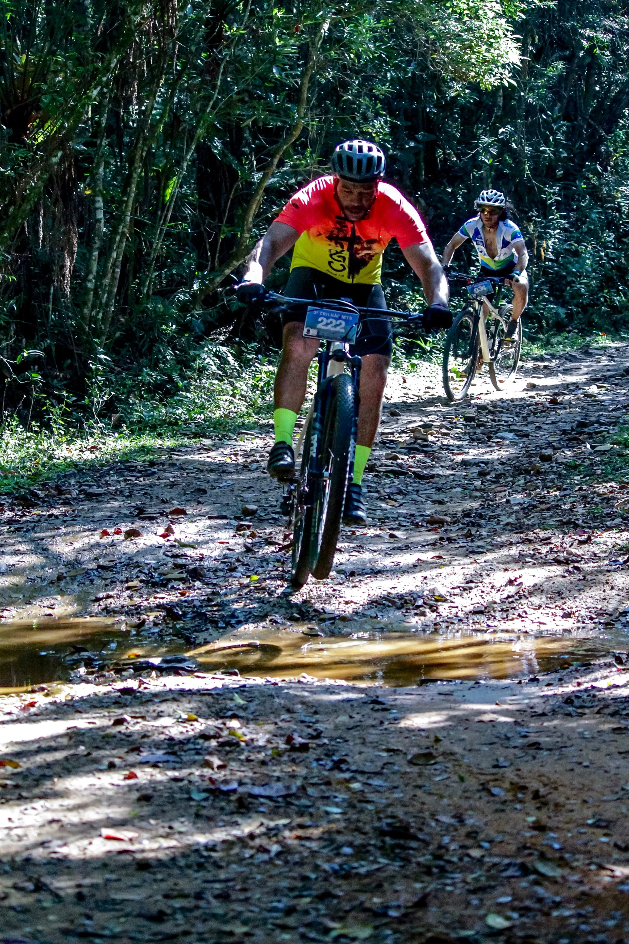 Atletas descendo trilha de floresta com lama após chuva