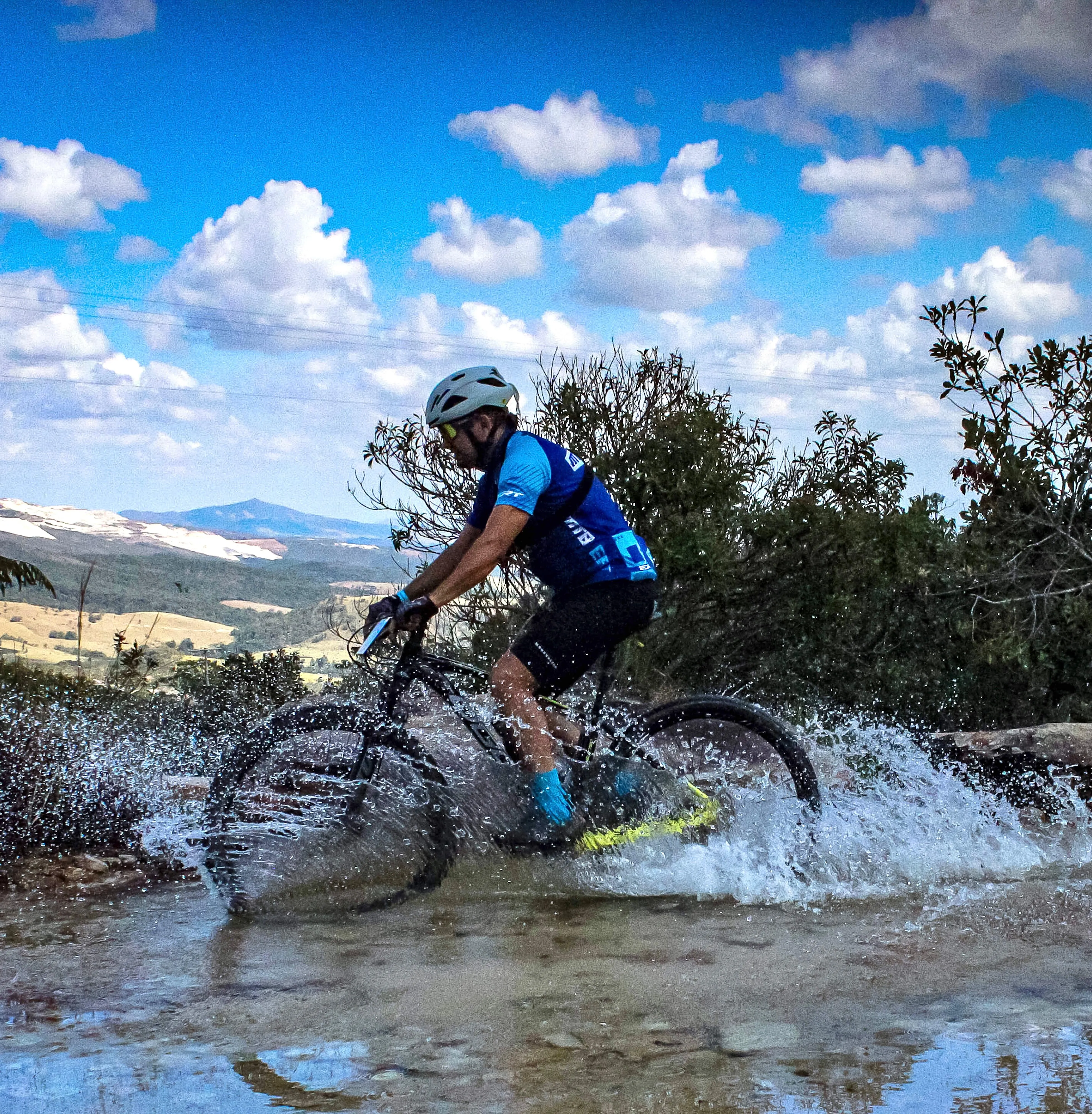 Ciclista cruzando trecho molhado com vista panorâmica do vale ao fundo
