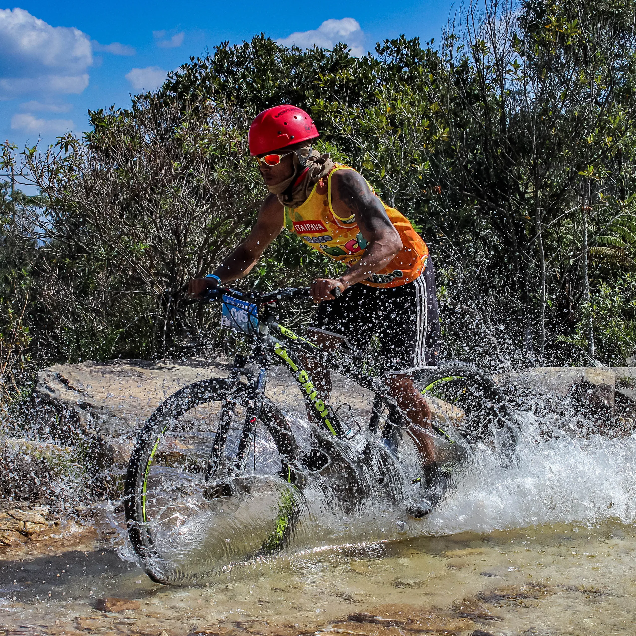 Ciclista cortando água em alta velocidade com capacete vermelho e céu azul