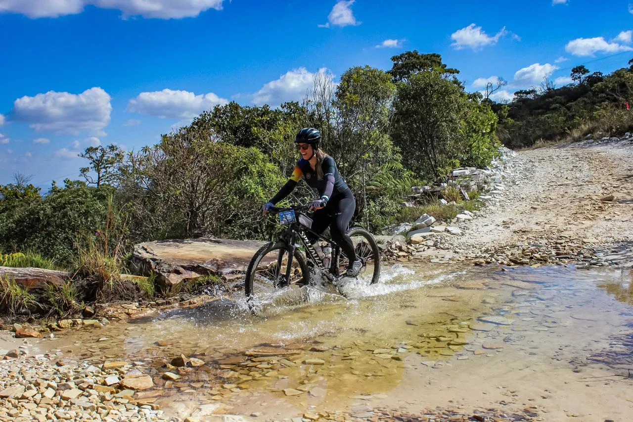 Atleta feminina atravessando riacho durante o percurso do Trilhão MTB